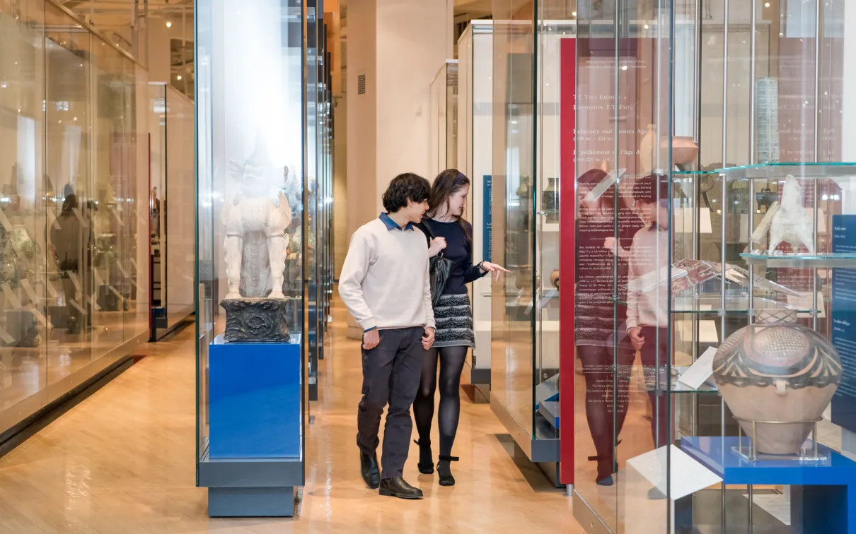 Two people wearing face masks looking at artifacts displayed in glass cases inside a museum gallery.