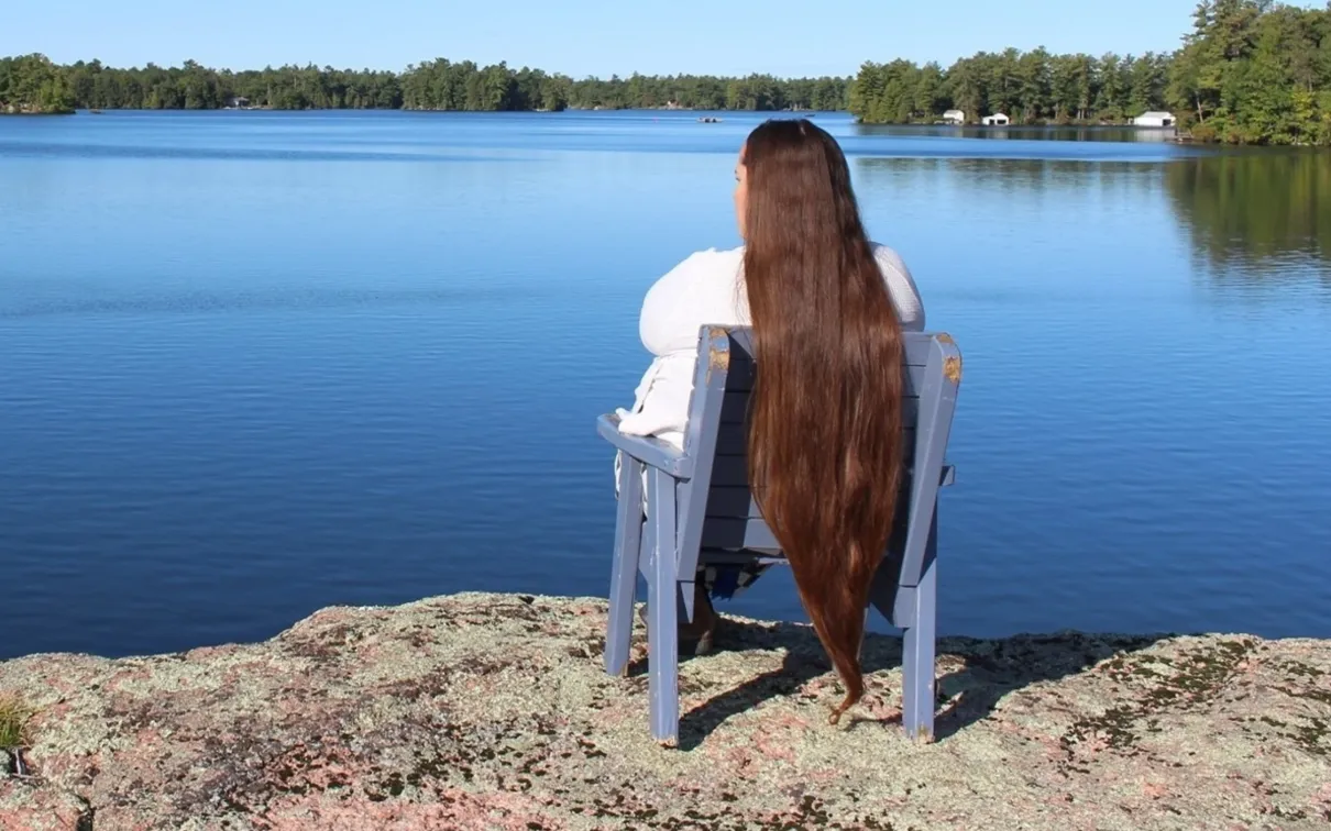 Une femme aux cheveux longs est assise sur une chaise surplombant un lac d'un bleu limpide.