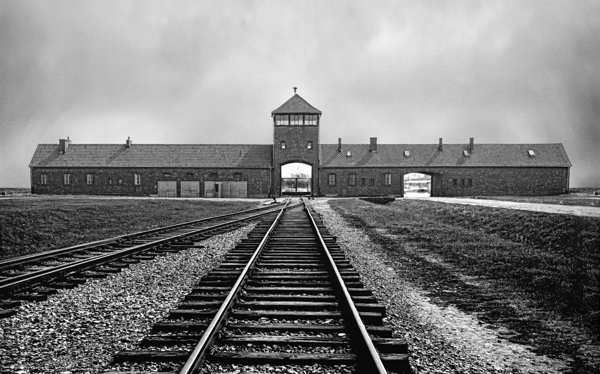 An entrance building at Auschwitz concentration camp with train tracks leading to its central archway.