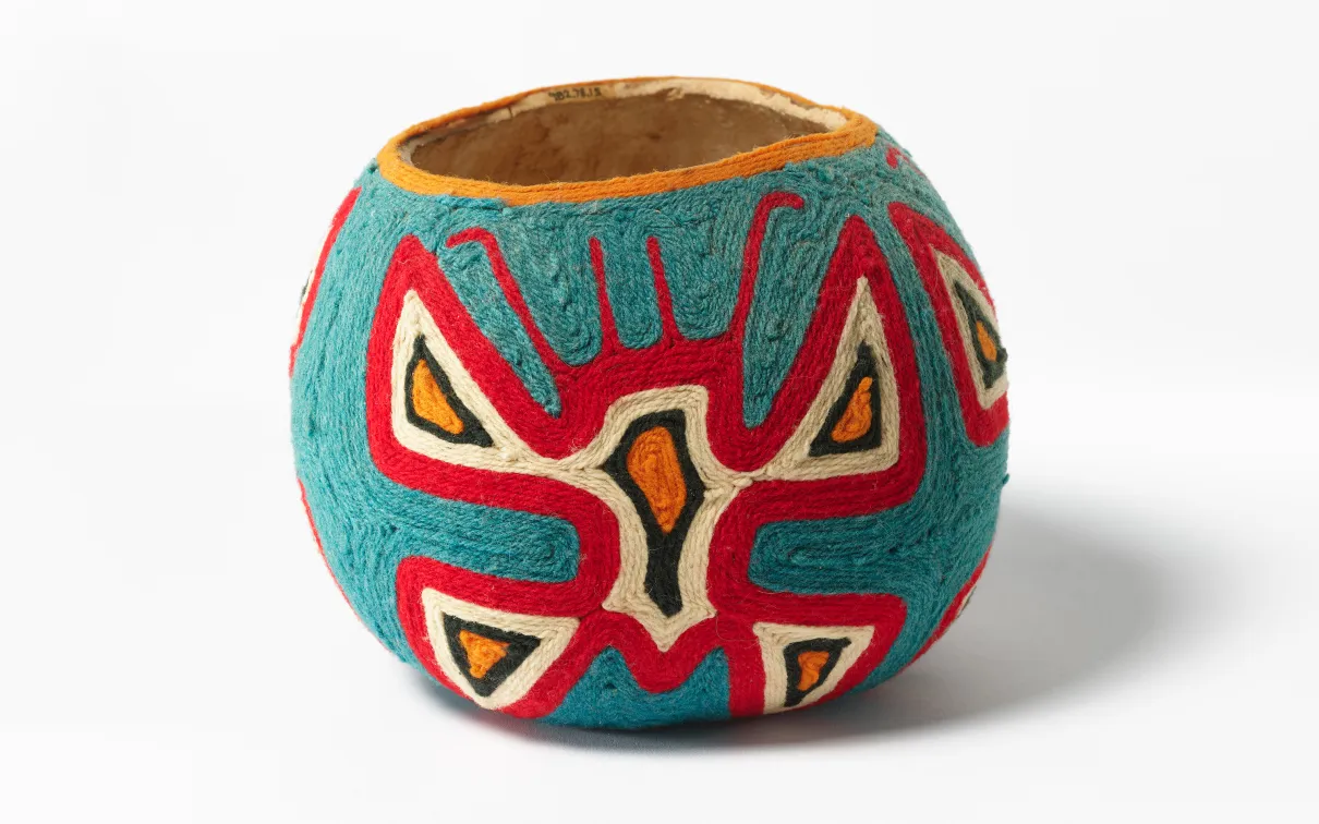 Small rounded vessel covered in blue fabric with red, white, black, and yellow decorative geometric patterns.