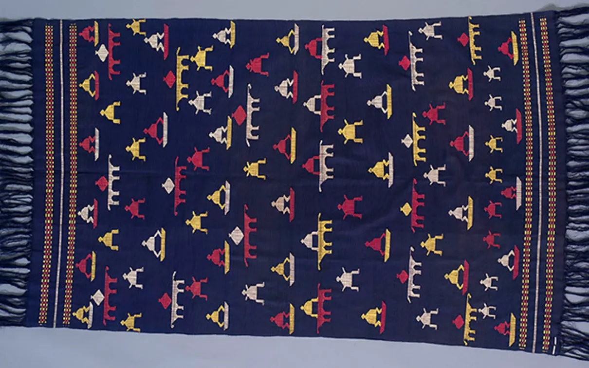 Woven textile with dark blue background and geometric patterns in red, yellow, white, and blue with fringed edges.
