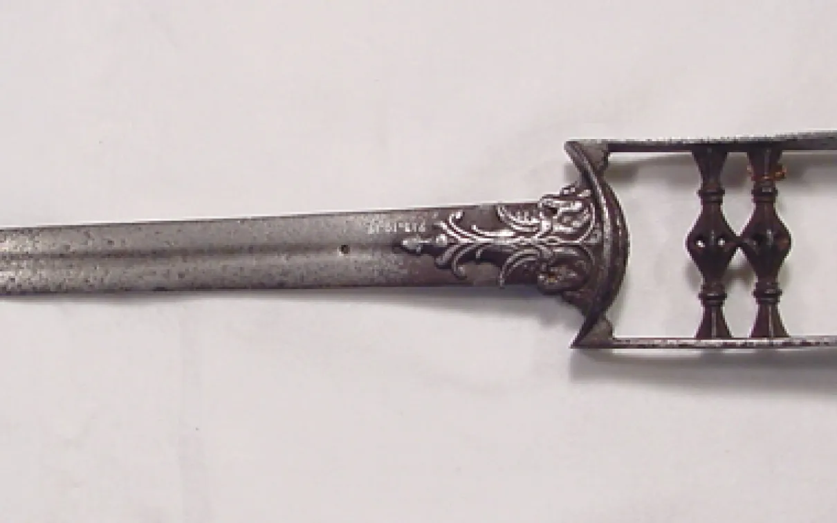 Metal two-pronged fork with ornamental handle featuring floral engravings.