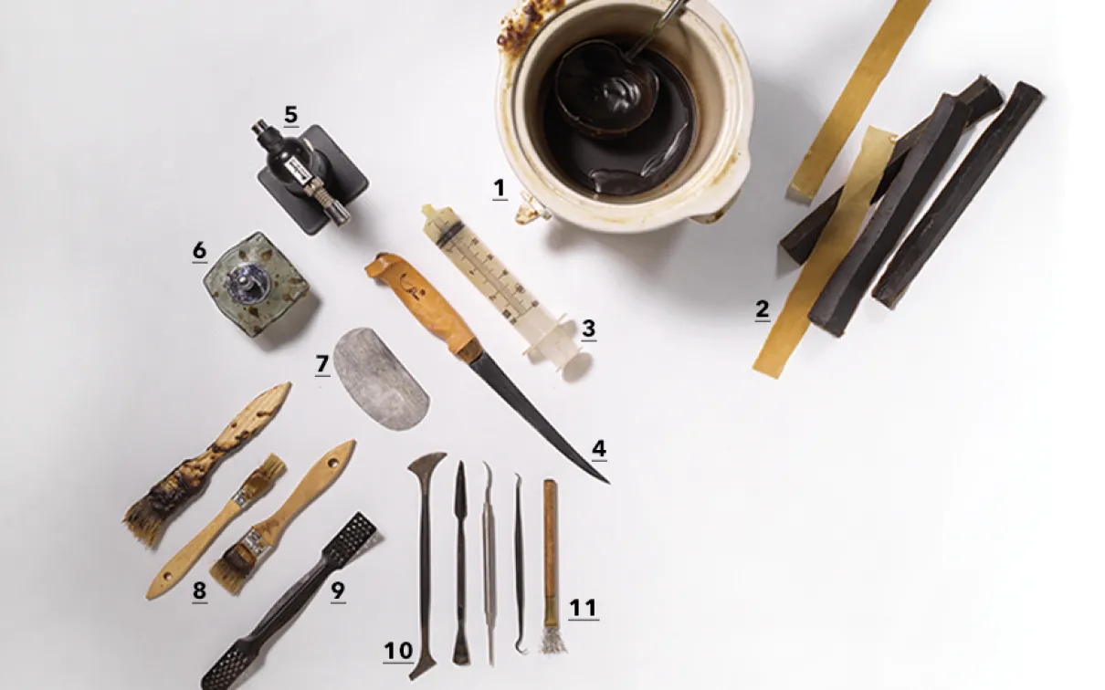 Divers outils traditionnels, dont des couteaux, des grattoirs et de petits objets sculptés, disposés sur une surface blanche à côté d'une tasse de café.
