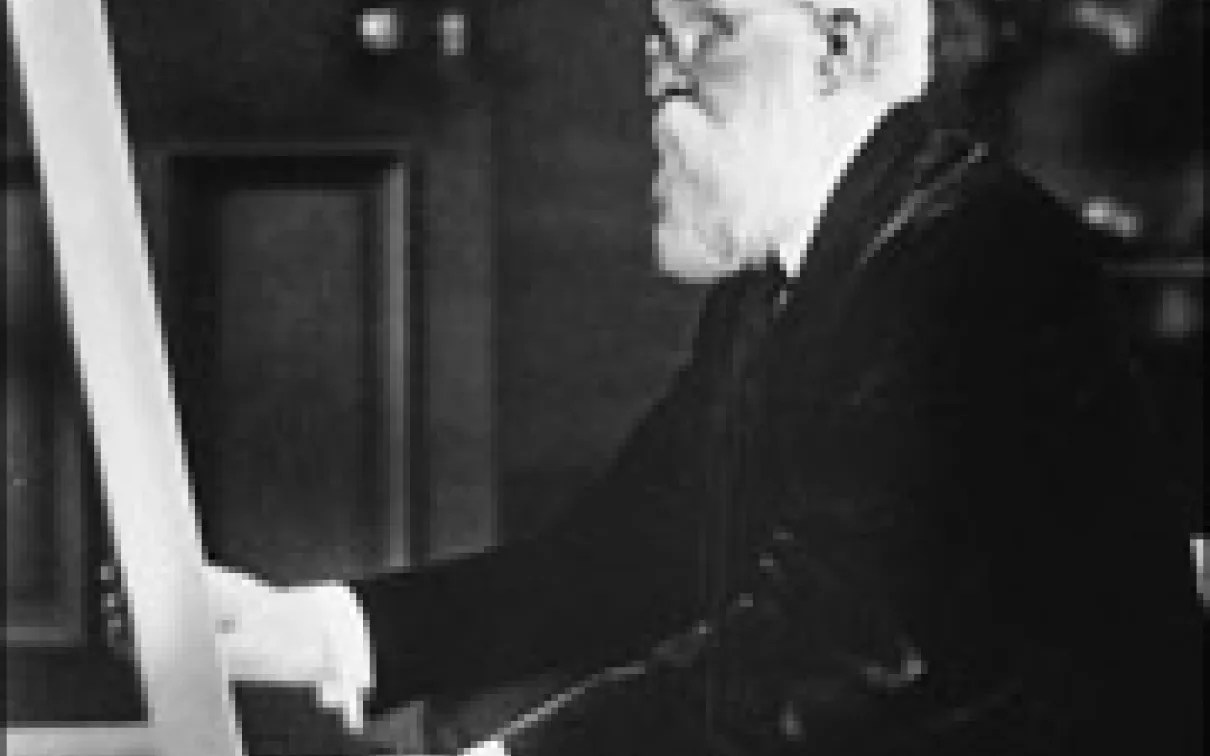 An elderly man with glasses and a beard examining a rolled-up document or blueprint.