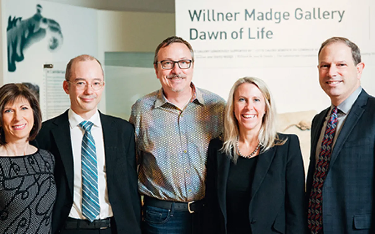 Five adults in business attire stand and smile in front of a sign reading “Willner Madge Gallery Dawn of Life.”