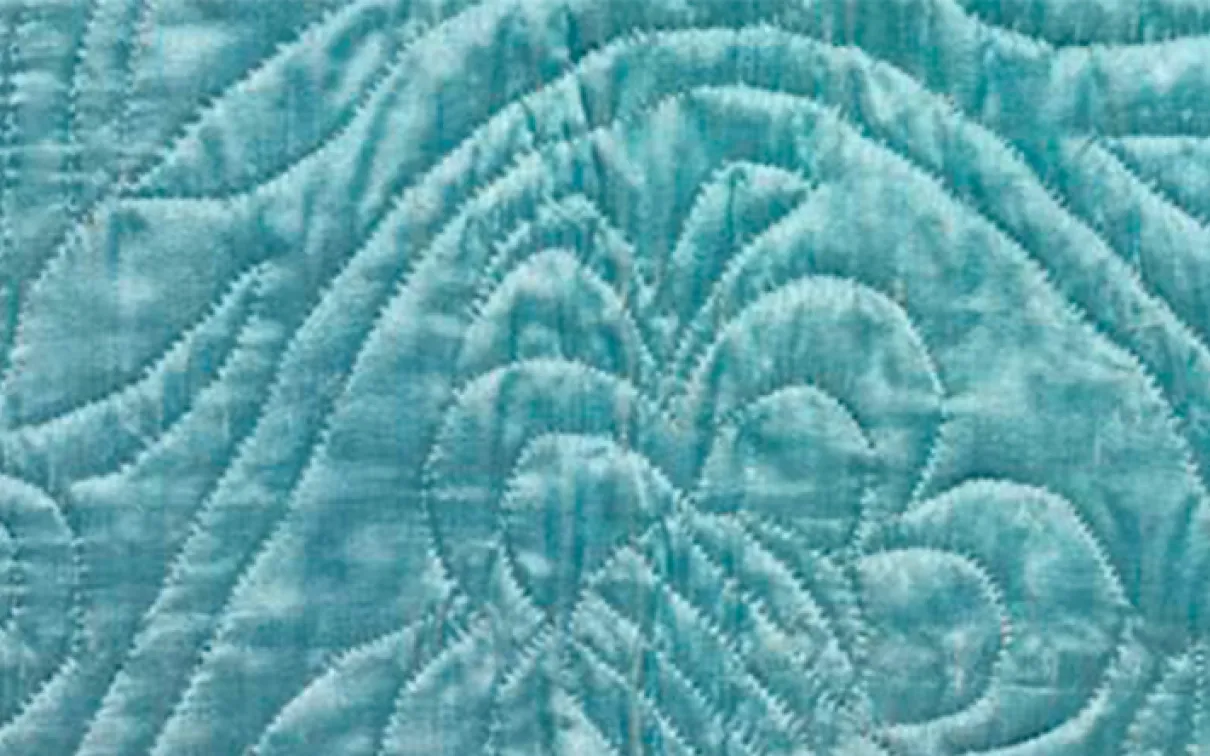 Close-up of a light blue fabric with stitched quilted patterns including a butterfly and symmetrical lines.