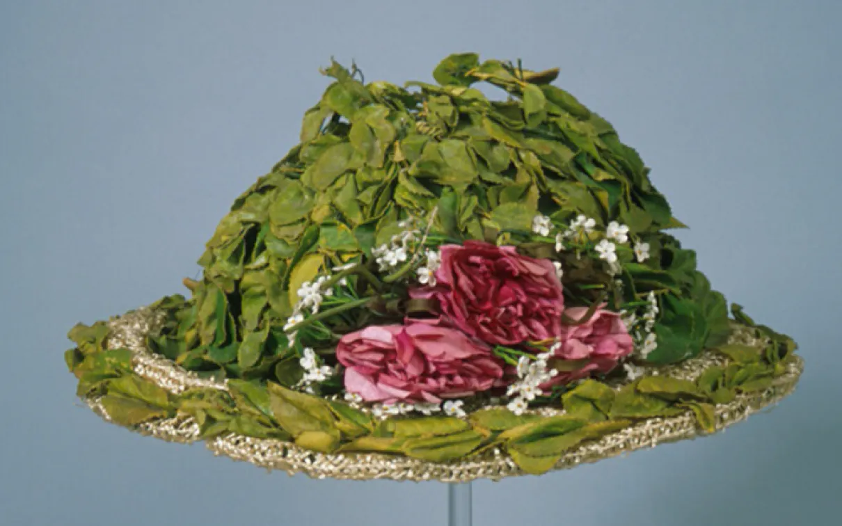 Green hat decorated with pink and white flowers and green leaves, with lace trim.