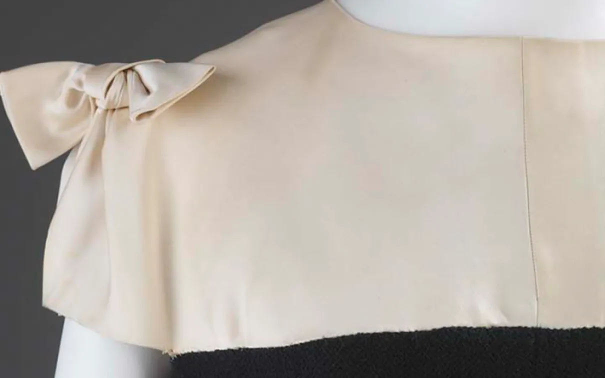 Close-up of an ivory dress bodice with a bow on the left shoulder.
