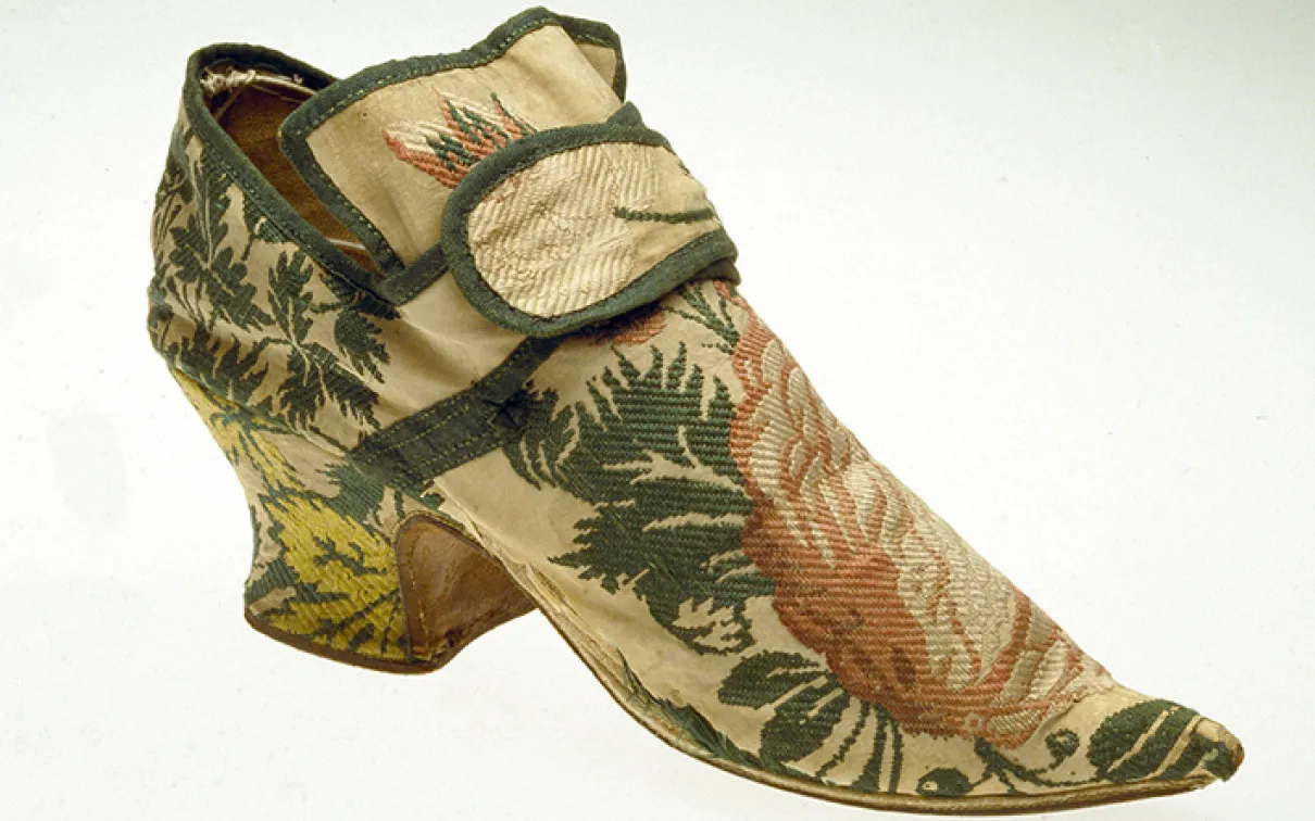 Chaussure en soie brodée du XIXe siècle avec des motifs floraux et de feuilles dans des tons verts, roses et jaunes.
