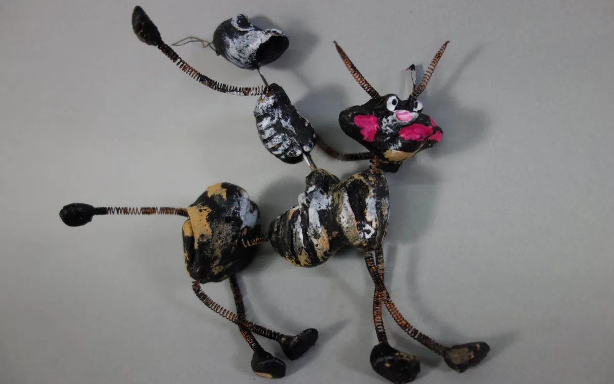 Small animal figure made of painted twigs and sticks on a gray background.