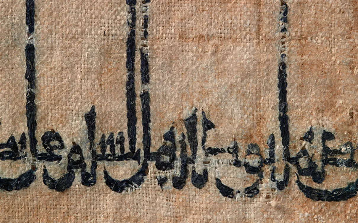 Écriture arabe à l'encre noire sur une surface havane et texturée, peut-être un parchemin ou un tissu.
