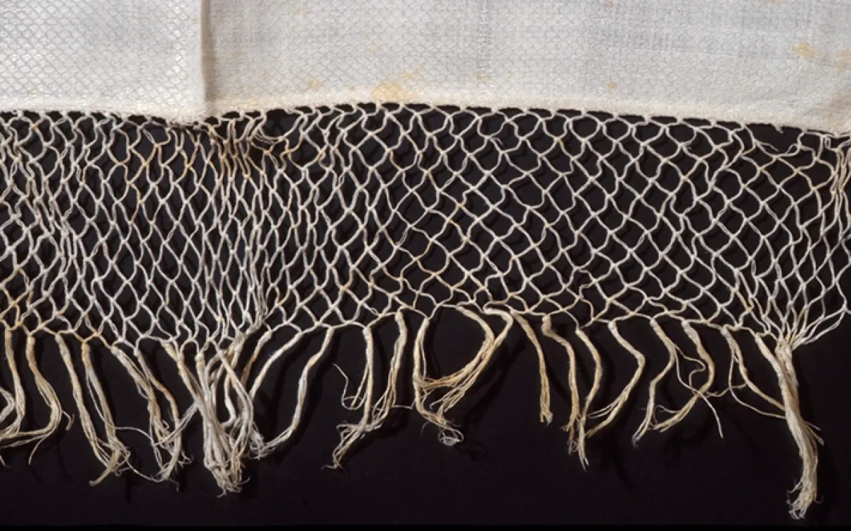 Close-up of beige woven net with knotted fringe on a black background.