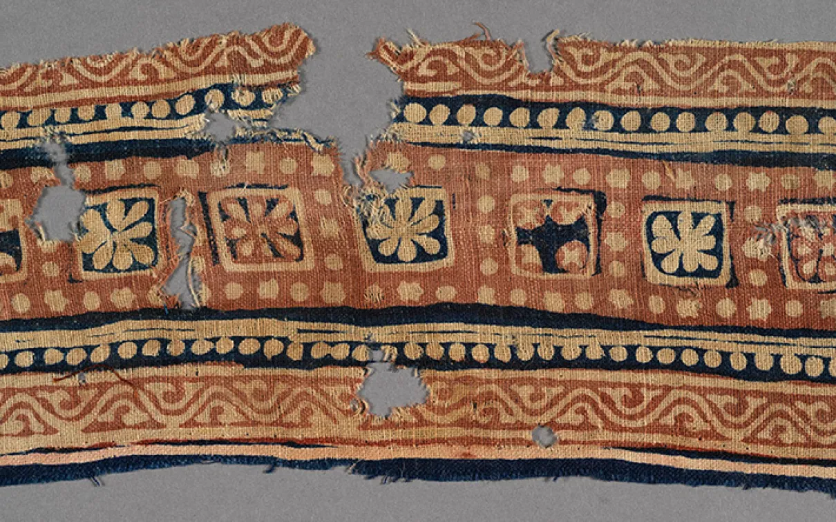 Decorative textile fragment with geometric and floral patterns in blue, beige, and red tones.
