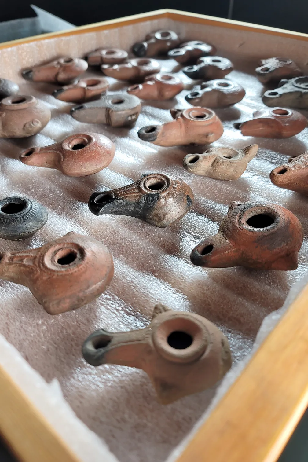 Tray displaying an assortment of small, ancient ceramic oil lamps arranged in rows.