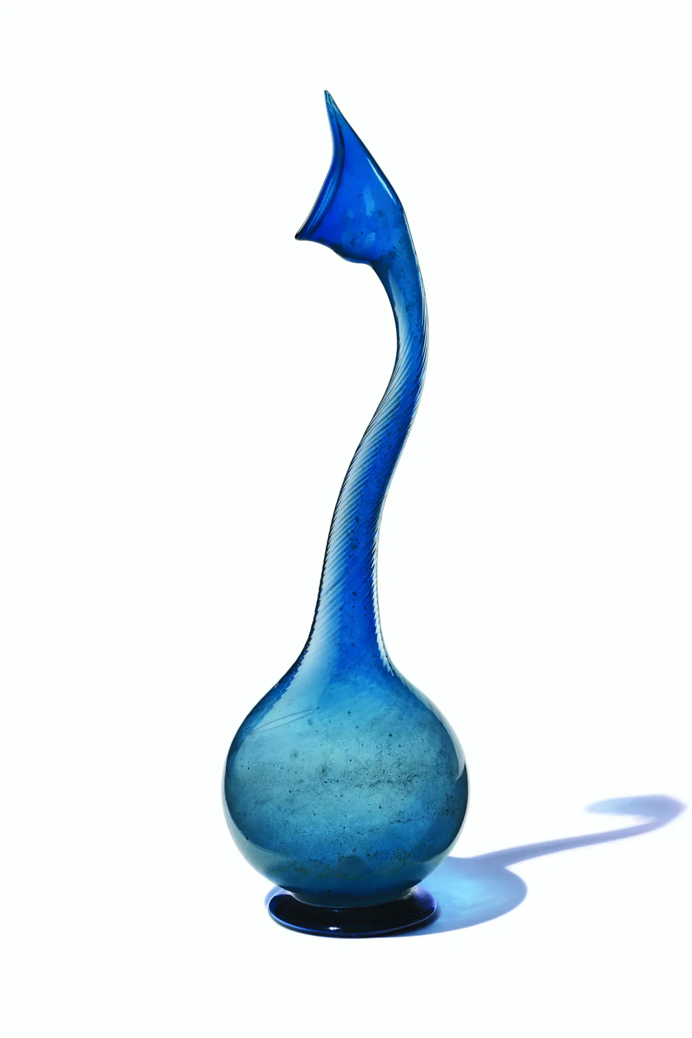 Grand vase élancé en verre bleu avec un col incurvé et une base bulbeuse qui projette une ombre.