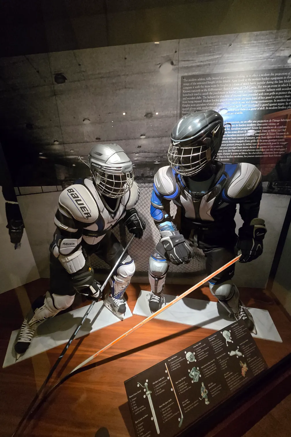 Deux mannequins vêtus d'équipements de hockey Bauer, y compris des épaulettes, des tibias, des gants, des patins et des casques. Les deux mannequins tiennent des crosses de hockey et prennent des poses dynamiques.