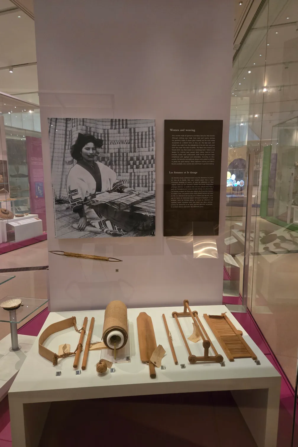 Dans la galerie d'un musée, une vitrine présente divers outils de tissage en bois.