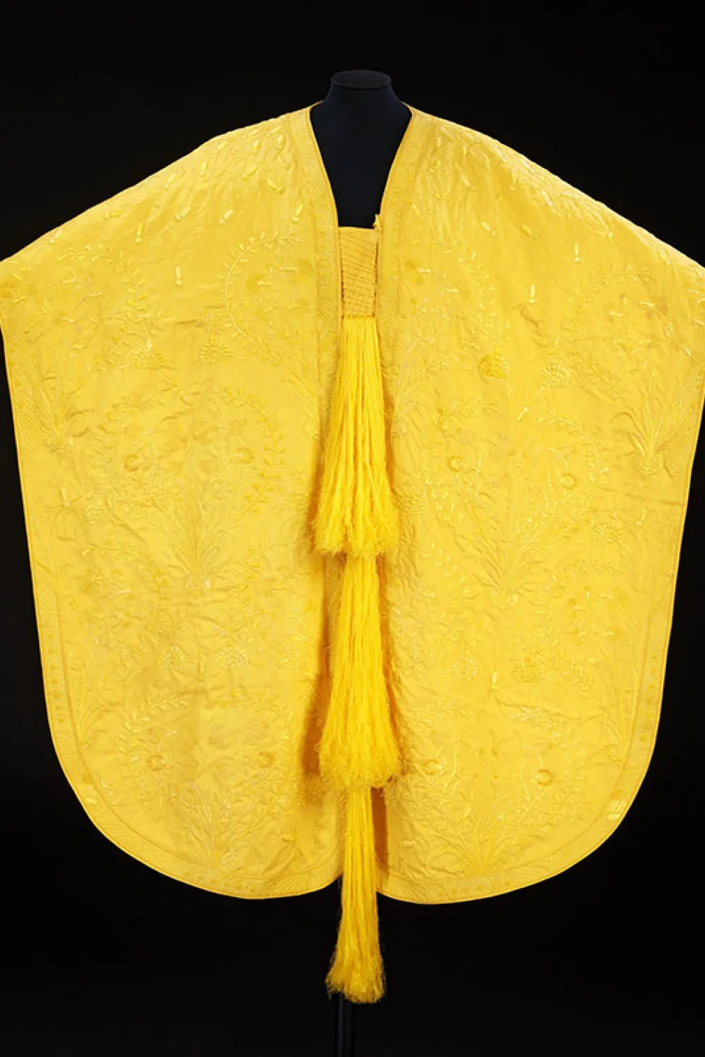 Yellow poncho with floral embroidery and three long tassels hanging down the front.