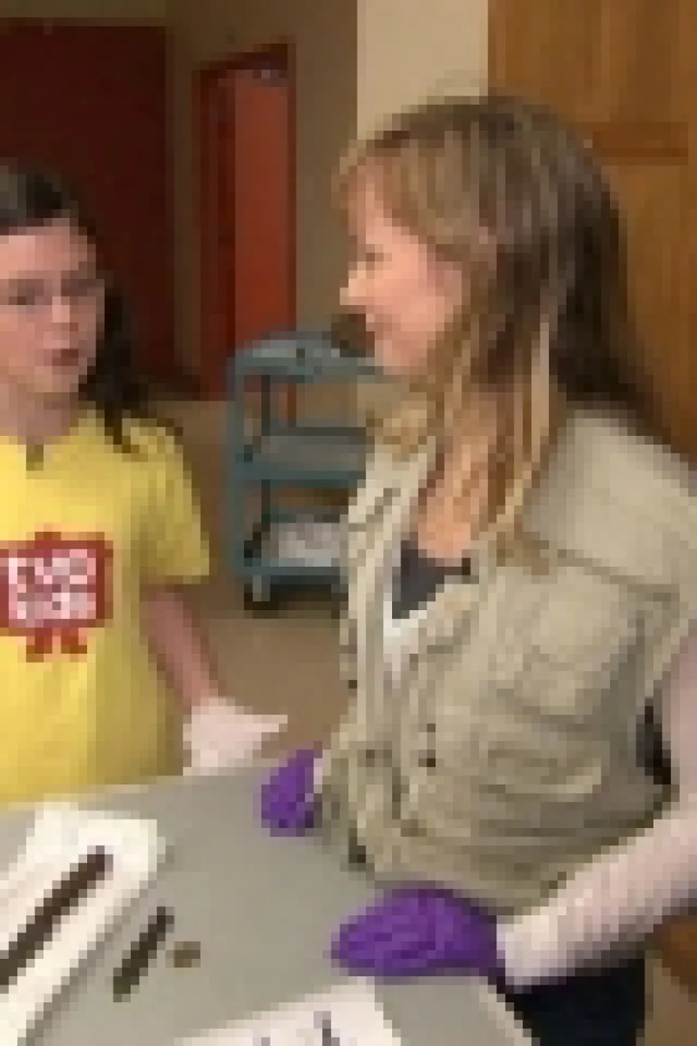 A young girl in a yellow T-shirt with "ROM" and a woman in a beige vest and purple gloves examine fossils on a table.