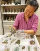 A woman in a pink shirt examines artifacts displayed in a white foam tray with labeled compartments.
