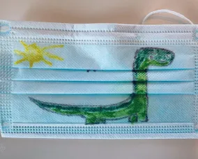 Blue disposable face mask painted with a green and brown dinosaur and a yellow sun in the top left corner.