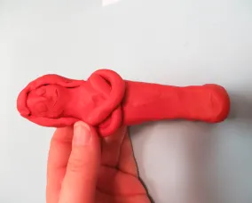 Hand holding a red clay sculpture resembling a human figure with a Head and torso.