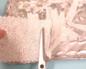 Hand holding a torn piece of white, maze-patterned paper next to a pair of black and white scissors cutting foil.