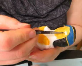 A person holding and painting a small penguin figurine with a fine paintbrush.