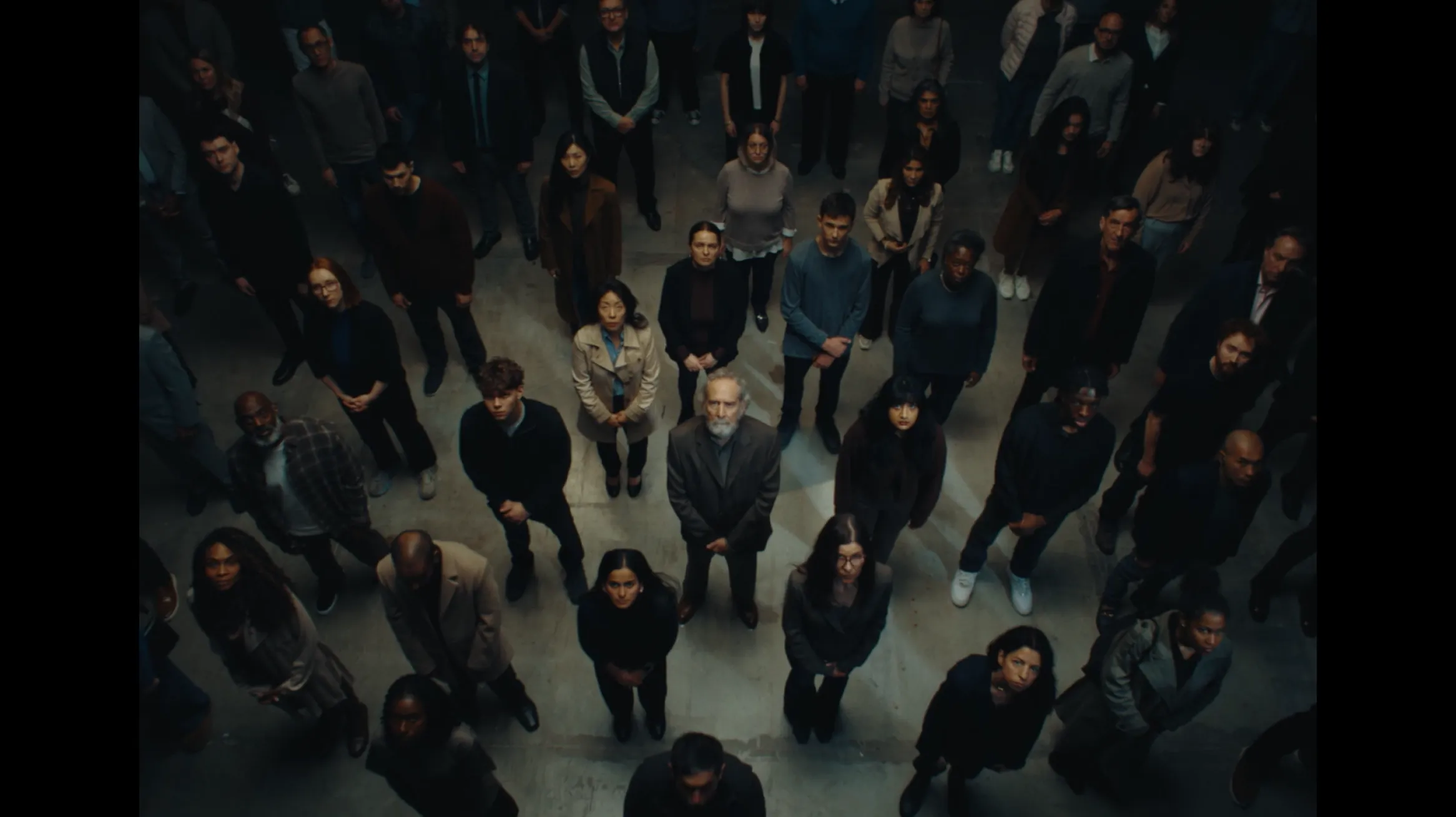 A group of people standing closely together, looking upward in a dimly lit space.